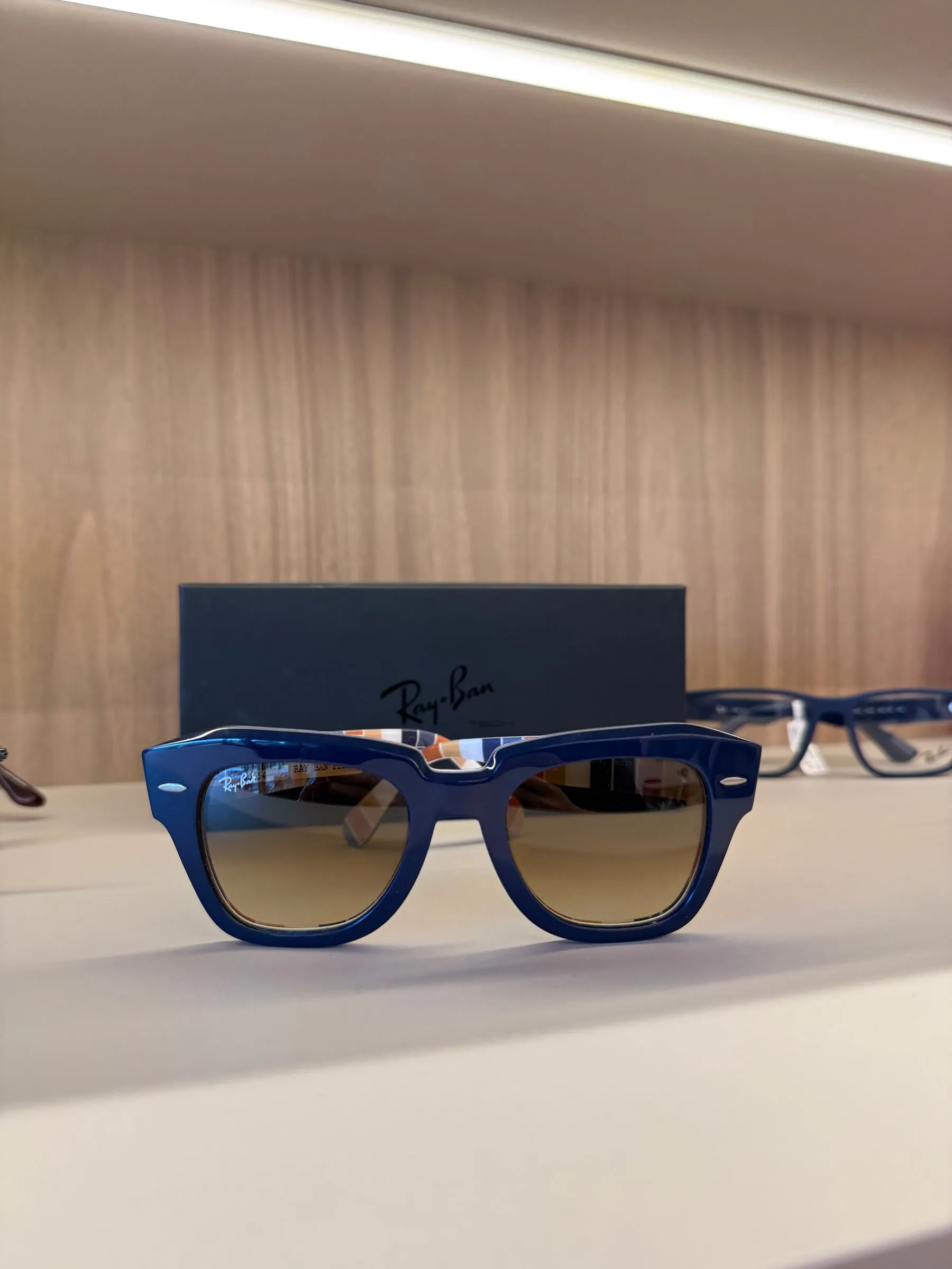 Óculos de sol Ray-Ban de armação azul e lentes em degradê, na frente da caixa da marca