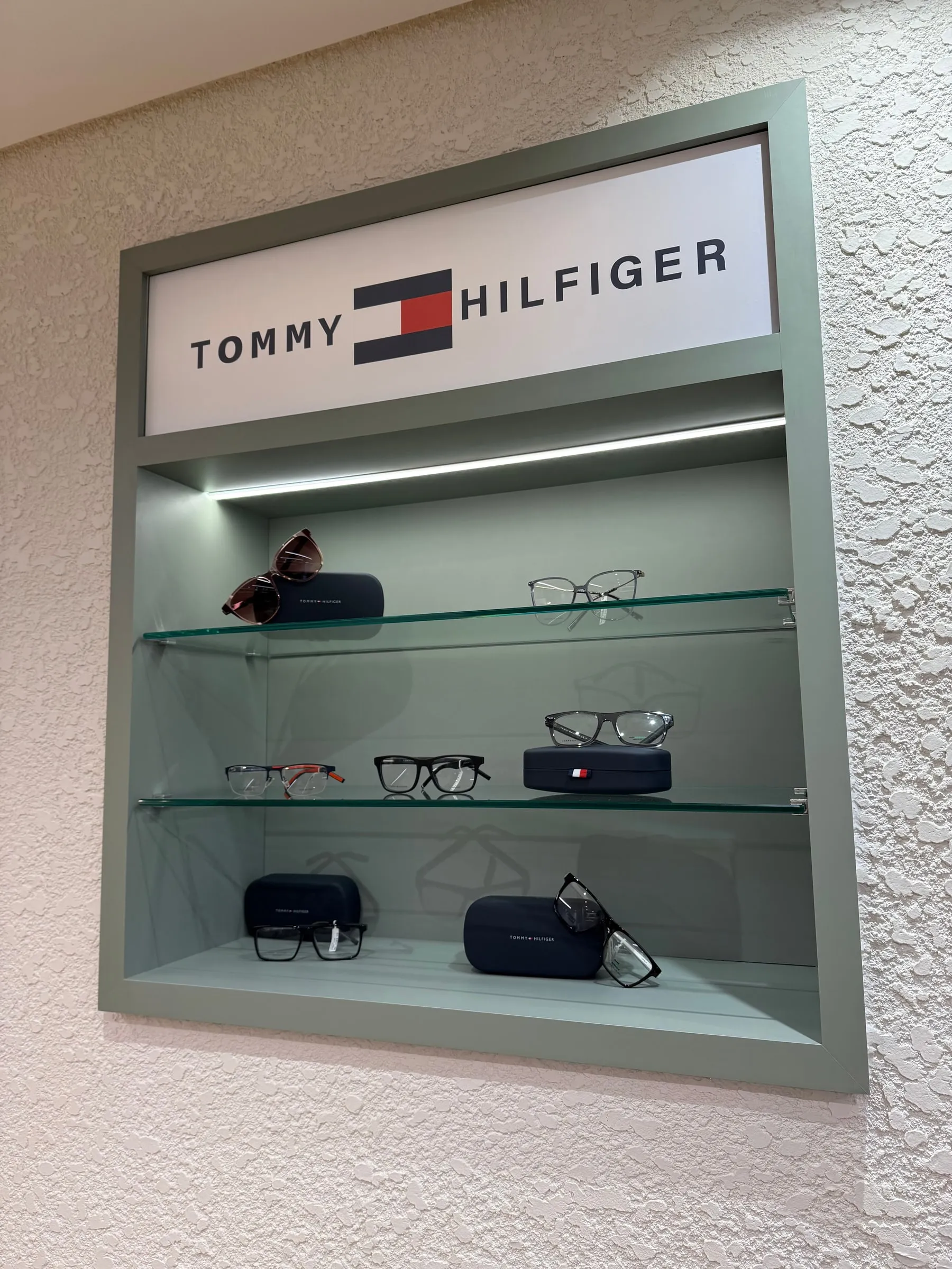 Nicho da Tommy Hilfiger com armações de grau, um óculos de sol e os estojos da marca